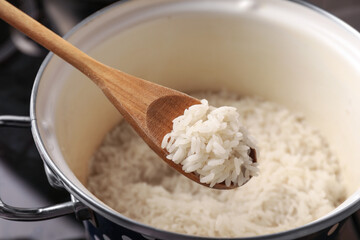 Wooden spoon with delicious rice over pot, closeup