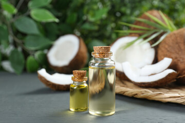 Bottles of organic coconut cooking oil and fresh fruits on grey table, closeup