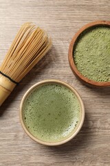 Cup of fresh matcha tea, bamboo whisk and green powder on wooden table, flat lay