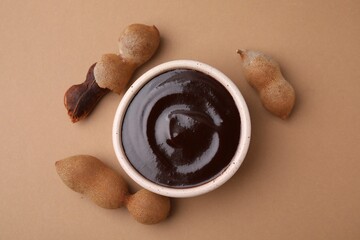 Bowl of tamarind sauce and fresh pods on light brown table, flat lay