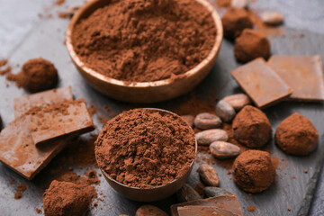 Bowls with cocoa powder, candies, beans and chocolate on black background