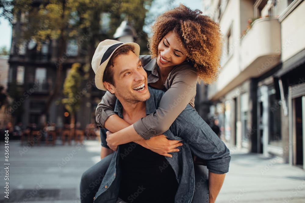 Wall mural young man carrying his girlfriend on his back while on a date in the city