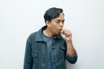 Portrait of Indonesian Asian man coughing and covering his mouth with hand clenched into a fist....