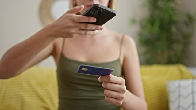 Young blonde woman make photo to credit card by smartphone at home
