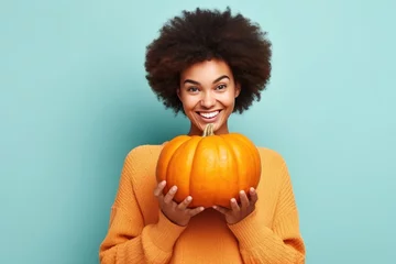  Attractive happy young black woman holding a pumpkin looking at the camera of cyan background © Adriana