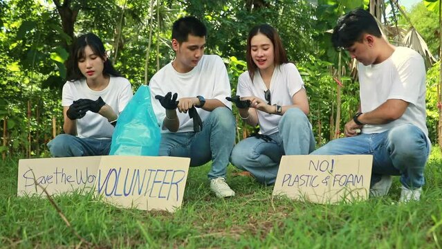 Group asian male and female volunteers sit wearing black gloves together cleaning preventing germs from dirt preparing pick up trash and preparing paper signs campaigning save the environment.