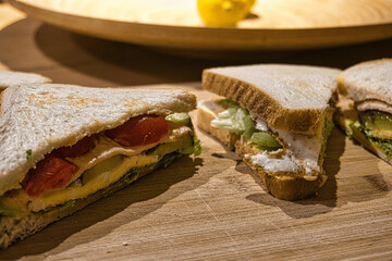 Foto von einem Sandwich mit Tomate, Ei, Gurke und Salat auf einem Brett mit Zahnstocher, in Scheiben geschnitten. Photo of a sandwich with tomato, egg, cucumber and lettuce on a board with toothpick