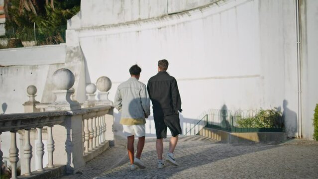 Lgbt lovers walking street holding hands at vacation. Mixed race gay couple love