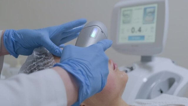 Hardware ultrasound cosmetic procedure in a beauty clinic. Skin rejuvenation, smas lifting anti-age therapy. Close-up beautician hands work with female patient face skin.