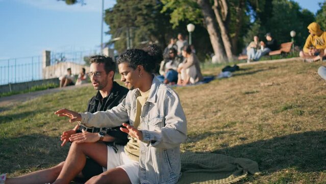 Happy bigender couple smiling talking on park lawn summer day. Happy gay family