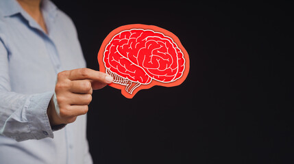 Close-up of hand holding a brain symbol made from red paper while standing on a black background.