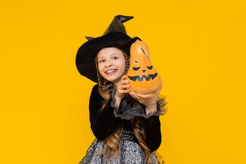 A little witch in a pointed hat holds an evil pumpkin. A child in a festive carnival costume on...