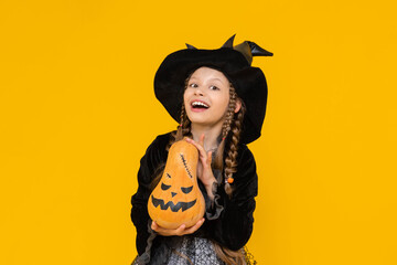 A little witch in a pointed hat holds an evil pumpkin. A child in a festive carnival costume on...