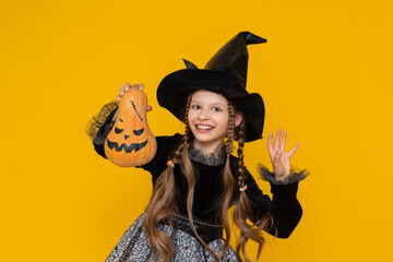 A little girl in a witch costume holds an evil pumpkin in her hands. Children's holiday carnival on...