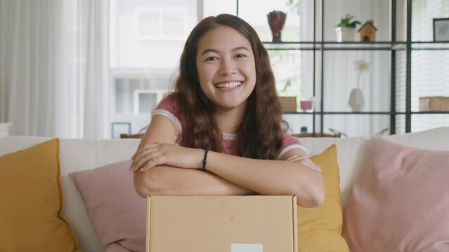 Young teen Gen Z girl asia people enjoy buy order gift postal parcel online shop. Happy receive courier carton box by fast express post mail omni channel retail store joy smile sitting at sofa home.