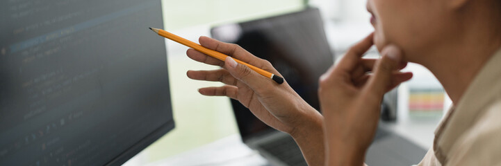 Developer programmer holds pencil and checking code on monitor while programming to developing web