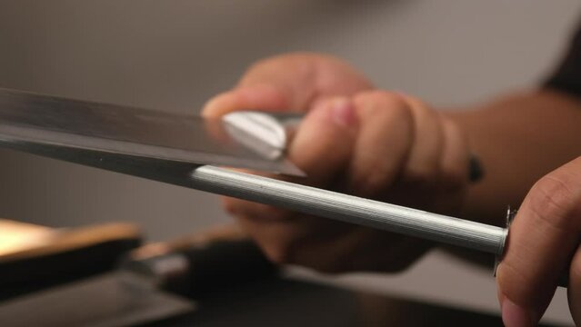 Close-up of female chef sharpening knives. Sharpen knives with a whetstone or grinding stone. Woman using a knife grinder, Hands sharpening knives in the kitchen.