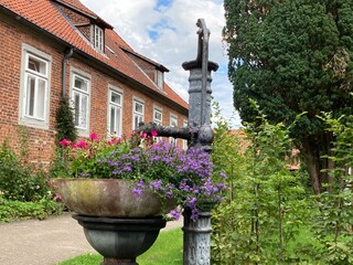 Alter Brunnen mit Blumen bepflanzt vor altem Gebäude im Kloster Walsrode mit Klostergarten in der Lüneburger Heide 