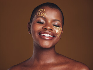 Gold, glitter and black woman smile from beauty with makeup and studio with sparkle cosmetics. Brown background, relax and female model with golden paint for skin glow and creative facial shine