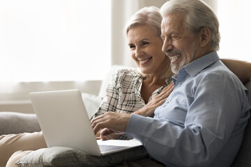 Happy elder married couple enjoying leisure, modern technology with digital gadget, resting on...