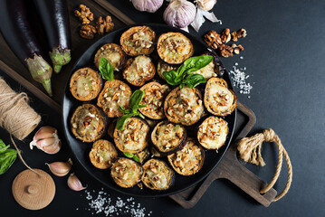 Appetizer of baked eggplant with garlic, cheese and walnuts on a black plate. Healthy homemade food