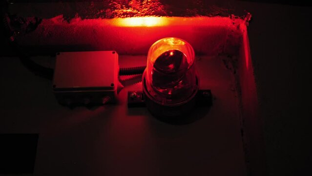 Close-up of a rotating red emergency siren lamp on the wall of a dark tunnel. A bomb shelter, an emergency signal on the wall during an air raid.