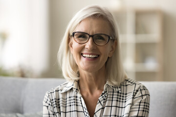 Cheerful beautiful blonde mature woman in trendy eyeglasses and casual shirt looking at camera,...