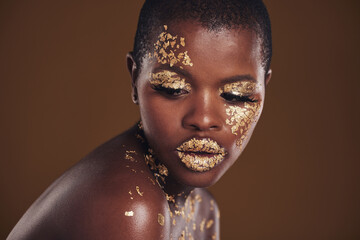 Art, studio and black woman with gold makeup on brown background, glitter paint facial and...