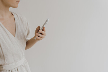 Mobile phone in female hands. Young pretty woman in neutral tan sandy beige linen dress