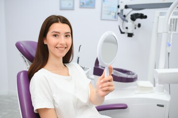 Pretty girl in dentist cabinet is using a mirror to look through the ideal work of a doctor.