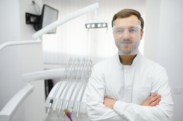 Fototapeta premium Attractive male dentist in doctors white lab coat posing in modern dental office