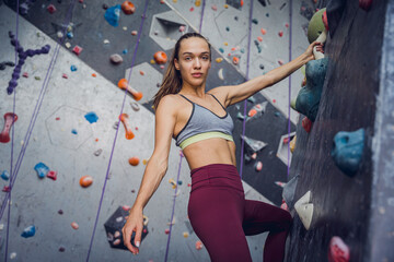 A strong female climber climbs an artificial wall with colorful grips and ropes.