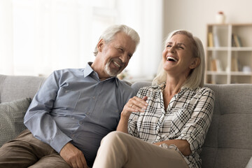 Cheerful elder husband and wife having fun at home together, relaxing on cozy couch at home,...