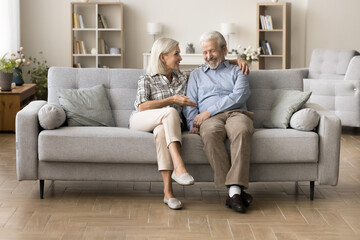 Happy older couple of grandparents enjoying leisure, conversation on home sofa together, talking,...