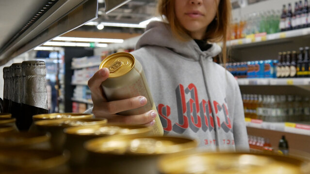 Close-up of a cute girl's hand taking a golden can of beer in a supermarket