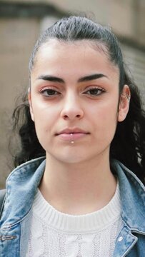 Vertical individual portrait of a young hispanic serious girl brunette student looking serious at camera. Juvenile teenage lady standing at university campus. Education concept. High quality footage