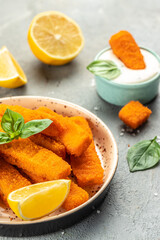 Crispy breaded deep fried fish fingers with breadcrumbs served with sauce and lemon. Food recipe background. Close up