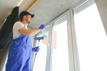 Male professional cleaning service worker in overalls cleans the windows.