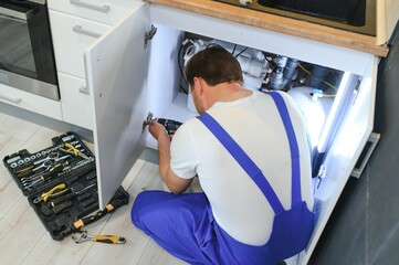Repairman In Overalls Repairing Cabinet Hinge In Kitchen