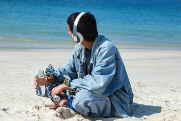 relaxed young man on the beach with headphones and drinking