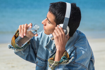 young hispanic latin man relaxing on the beach with headphones and drinking