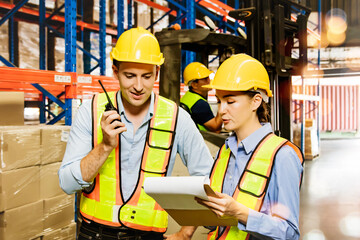 Professional warehouse team in white safety clothes of men and women working in warehouse holding walkie talkies and documents checking package piles shelves and forklift operators moving goods.