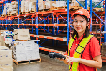 Beautiful Asian female worker working wearing working helmet with smiling face check boxes by scanning bacode from warehouse shelves to verify authenticity.