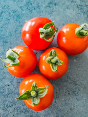 Five small red tomatoes on a grey background 