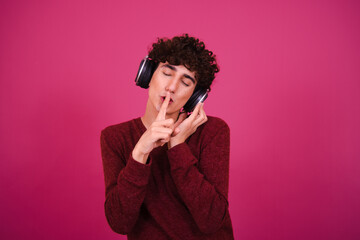 Funny attractive guy listens to music in headphones. Pink background.