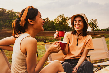 Wonderful evening moment : Two asian female friends sitting and chatting cheerfully drinking...