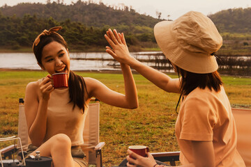 Wonderful evening moment : Two Asian girlfriends high fives sat and chatted happily drinking...