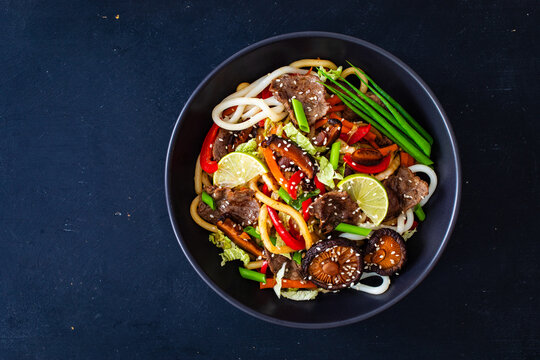 Asian food - roast beef, noodles and stir fried vegetables on wooden table
