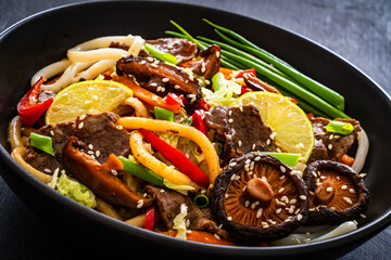 Asian food - roast beef, noodles and stir fried vegetables on wooden table
