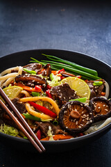 Asian food - roast beef, noodles and stir fried vegetables on wooden table

